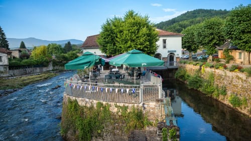 Terrasse riverside de la Maison du Haut Salat avec parasols verts dominant la rivière Salat à Seix, France