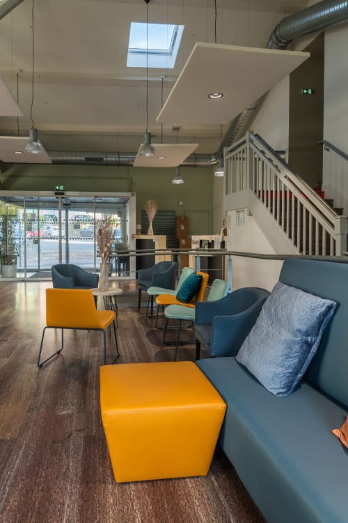 Hall d'hôtel moderne à la Maison Du Haut Salat avec poufs jaunes, sièges bleus, lumière naturelle et escalier à Seix, France.