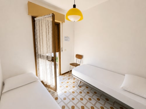 Camera da letto doppia luminosa all'Hotel Anthea a Lignano Sabbiadoro con pavimento decorato, lampada sospesa gialla e vista sul giardino