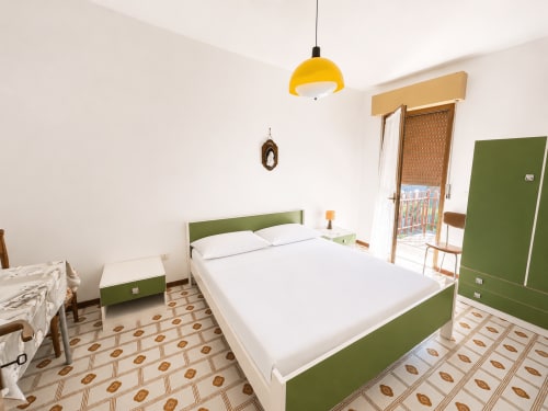 Camera moderna dell'hotel Anthea a Lignano Sabbiadoro, con letto verde, lampada a sospensione gialla e balcone con vista sul giardino