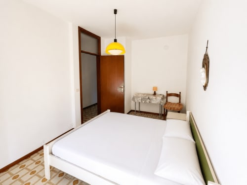 Luminosa camera d'albergo Anthea a Lignano Sabbiadoro con letto bianco, lampada a sospensione gialla e accesso alla vista del giardino