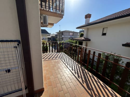 Terrazza soleggiata della Villa Loris 3 all'hotel Anthea, Lignano Sabbiadoro, con ringhiere in legno e vista sul giardino