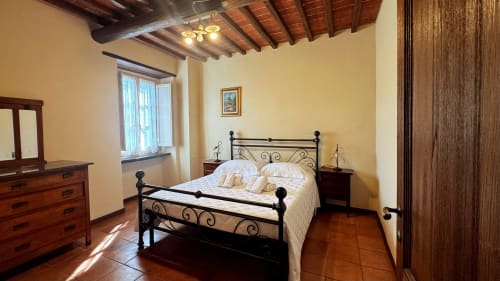 Bright bedroom at Borgo di Erboli BnB in Cavriglia with wrought iron bed, wooden beams, and traditional furnishings