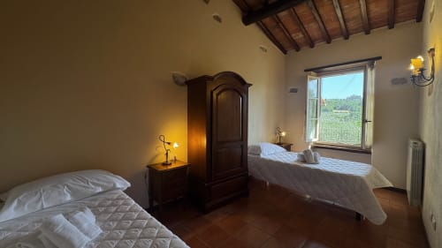 Spacious family apartment bedroom at Borgo di Erboli in Cavriglia with two beds, wooden furnishings, and hillside views