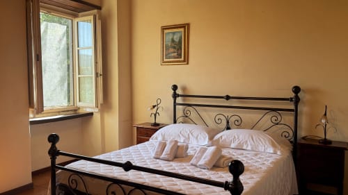 Bright bedroom in Borgo di Erboli apartment with wrought iron bed, cream bedding, wooden nightstands, and window with
