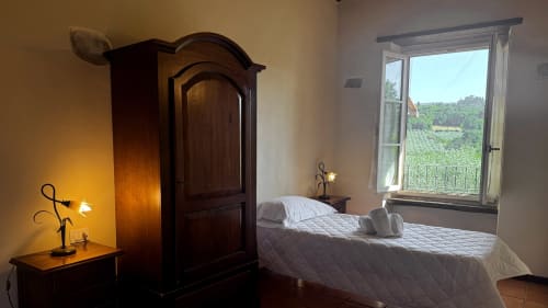 Rustic bedroom at Borgo di Erboli with wooden wardrobe, white bed, and window overlooking Tuscan countryside