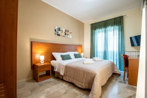 Luminosa camera familiare a La Zagara Rooms a Milazzo con vista sul mare, letto in legno, tende verdi e comfort moderni