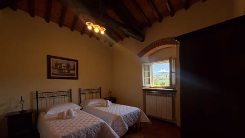 Family apartment bedroom at Borgo di Erboli in Cavriglia with twin beds, terracotta beams, and countryside views