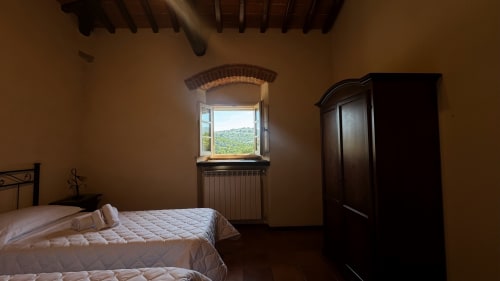 Rustic bedroom at Borgo di Erboli in Cavriglia with exposed beams, twin beds, and countryside views through arched window