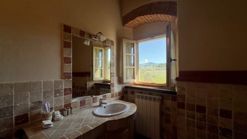 Rustic bathroom at Borgo di Erboli, Cavriglia with terracotta tiles, round sink, and countryside window views
