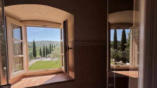 Open wooden window in Borgo di Erboli apartment overlooking Tuscan countryside with cypress trees and green hills near