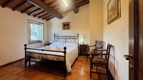 Rustic bedroom at Borgo di Erboli in Cavriglia with wrought iron bed, wooden beams, and terracotta floors