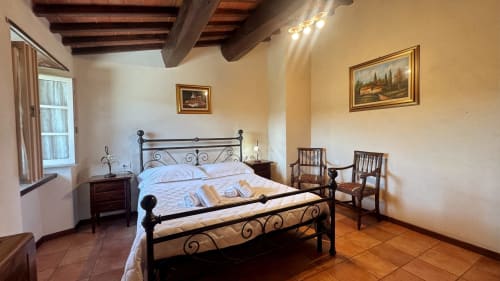Family apartment bedroom at Borgo di Erboli in Cavriglia with wrought iron bed, terracotta floors, and rustic wood beams