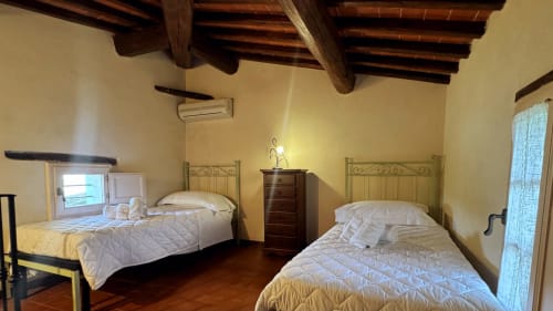 Family apartment bedroom at Borgo di Erboli in Cavriglia with two beds, wooden beams, and rustic decor