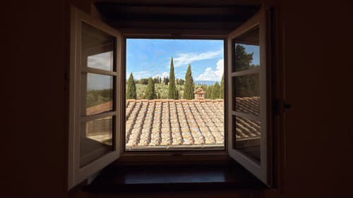 Open window at Borgo di Erboli revealing Tuscan vineyard, cypress trees, and countryside villa in Cavriglia