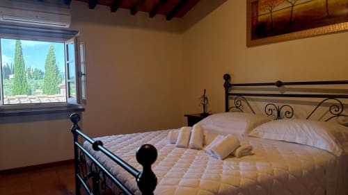 Bedroom at Borgo di Erboli in Cavriglia with wrought iron bed, white linens, and window view of cypress trees