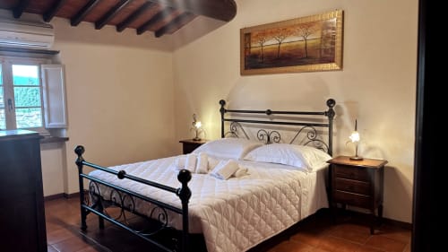 Elegantly furnished bedroom at Borgo di Erboli, Cavriglia, with iron bed frame, white bedding, wooden nightstands, and warm