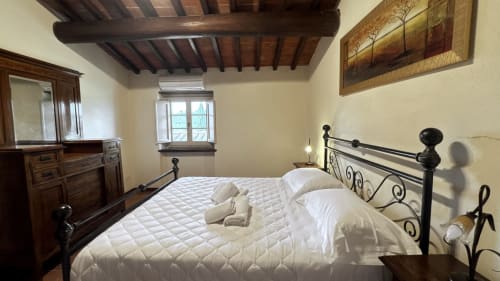 Spacious family apartment bedroom at Borgo di Erboli, Cavriglia, with wrought iron bed, exposed wooden beams, and rustic
