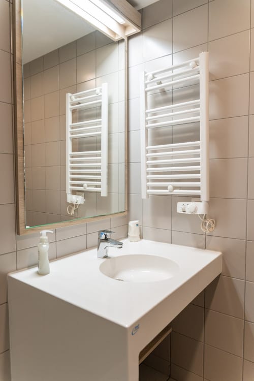 Salle de bain moderne à Maison Du Haut Salat avec lavabo blanc, miroir et sèche-serviettes chauffants dans une pièce aux carreaux beige