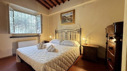 Bright bedroom at Borgo di Erboli in Cavriglia with wrought iron bed, wooden beams, and terracotta floors