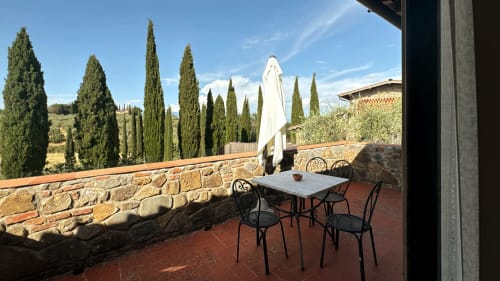 Terrace at Borgo di Erboli with cypress trees, stone walls, and dining furniture overlooking Cavriglia countryside