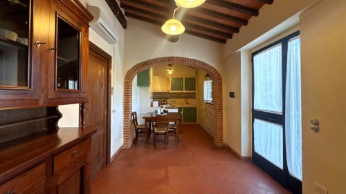 Rustic apartment hallway at Borgo di Erboli with terracotta floors, exposed beams, and brick archway leading to kitchen