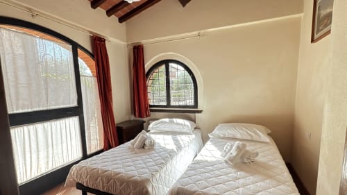 Two twin beds in bright Borgo di Erboli apartment with arched window and red curtains, Cavriglia