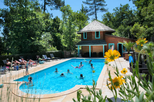 Des clients se détendent à la piscine turquoise de Nature et Océan à Messanges - lodge en brique avec fleurs jaunes et vue sur la forêt