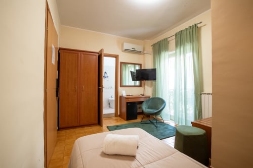 Camera luminosa a La Zagara Rooms a Milazzo con letto bianco, sedia verde, TV e bagno privato
