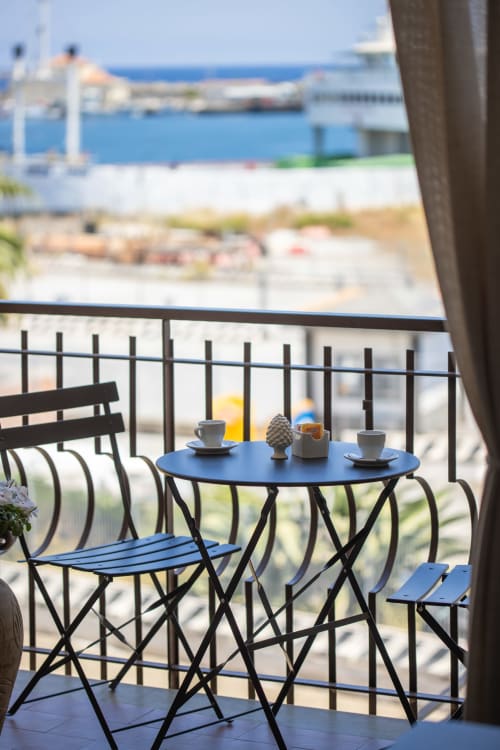 Balcone fronte spiaggia a La Zagara Rooms a Milazzo con tavolo blu, servizio caffè e vista sul porto