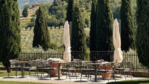 Outdoor terrace at Borgo di Erboli with dining chairs, umbrellas, cypress trees and Tuscan landscape views