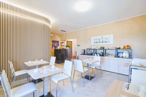 Moderna sala colazione della La Zagara Rooms B&B a Milazzo con tavoli da pranzo, sedie bianche e zona cucina