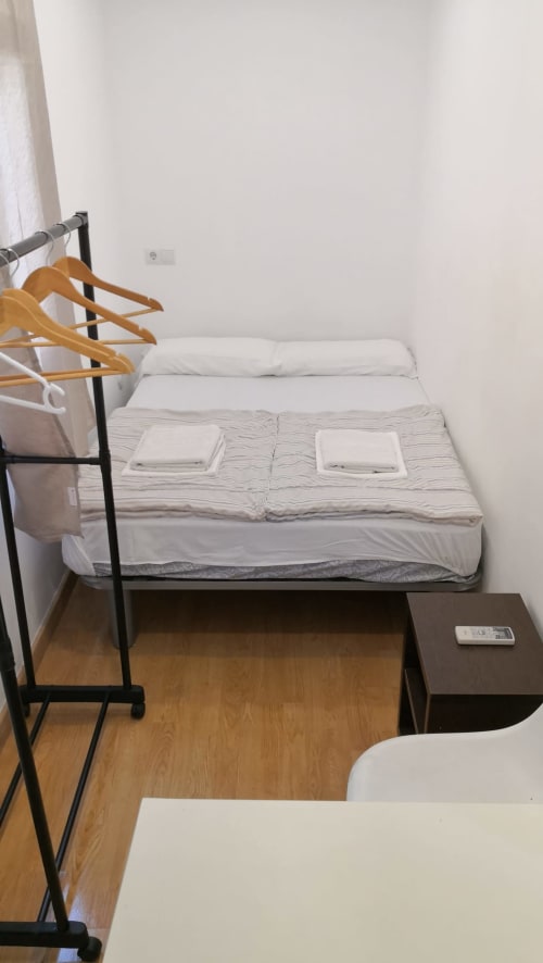 Habitación de Hostal Porto Mar en Salou con cama de madera, ropa de cama blanca, dos almohadas, perchas de madera y mesita oscura