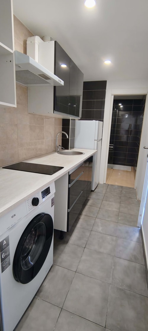 Cocina moderna con muebles blancos, electrodomésticos negros, lavadora y piso de azulejos en Hostal Porto Mar, Salou
