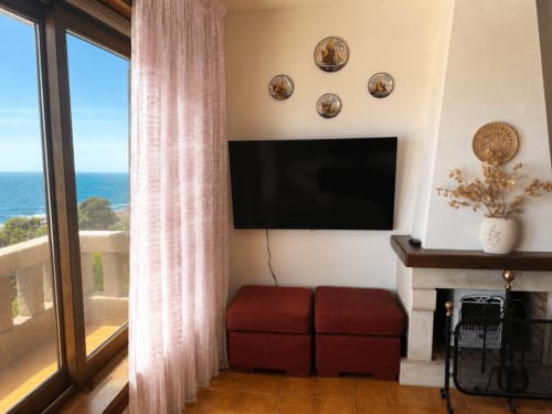 Salón luminoso en la villa Vila Mar de Lua, Oia, con vistas al mar a través de la puerta del balcón, puffs rojos, TV de pared, y