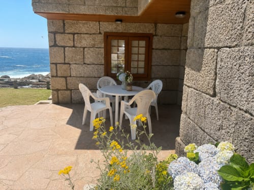 Terraza de villa frente al mar en Oia con mobiliario de comedor blanco, flores amarillas y blancas, muros de piedra y vistas al mar