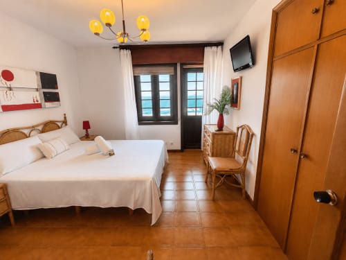 Dormitorio luminoso en Vila Mar de Lua en Oia con vista al mar, cama de madera, muebles de ratán y balcón con vistas al océano