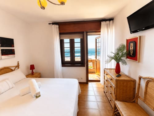 Dormitorio de villa de playa en Oia con puertas con vista al mar, cama blanca, muebles de madera y balcón con vista al océano