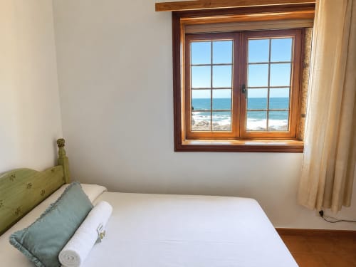 Dormitorio luminoso con vistas al mar a través de ventanas con marco de madera en la villa Vila Mar de Lua en Oia, España