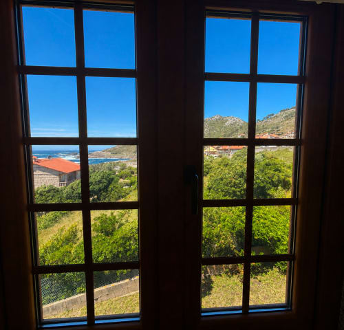Vista desde Villa Mar de Lua en Oia mostrando el mar Mediterráneo, colinas costeras y exuberante vegetación a través de ventanas con marco negro
