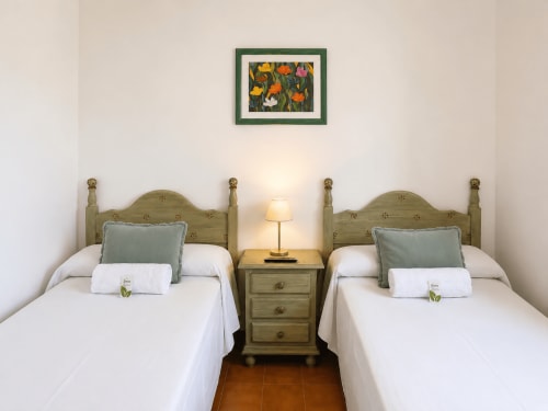 Dos camas con cabeceros verdes en villa Vila Mar de Lua, Oia. Ropa de cama blanca, almohadas verdes, mesita de noche de madera con lámpara.