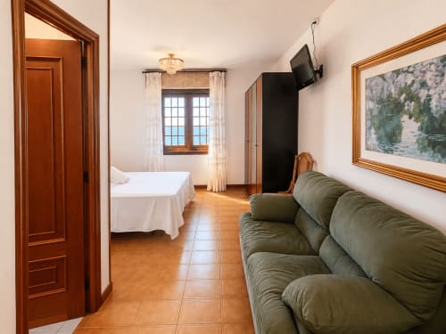 Amplia sala de estar de villa con vistas al mar en Oia, sofá verde, cama, puertas de madera y arte enmarcado