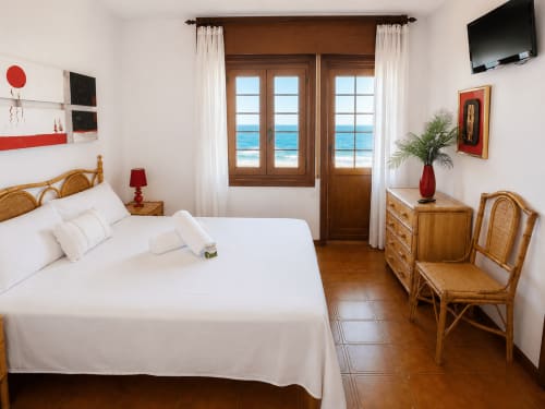 Dormitorio de villa frente al mar en Oia con vistas al océano, muebles de madera, ropa de cama blanca y puertas orientadas al mar en Holibai