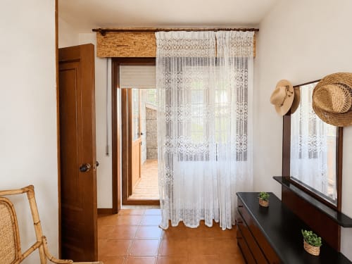 Habitación luminosa en villa Vila Mar de Lua, Oia con cortinas de encaje, muebles de madera, sombreros de paja y acceso a vista al mar