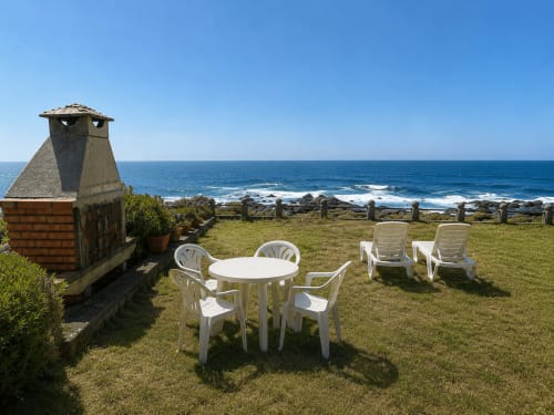 Terraza de villa frente al mar en Holibai Oia con muebles blancos, chimenea y vistas al océano sobre olas y costa rocosa
