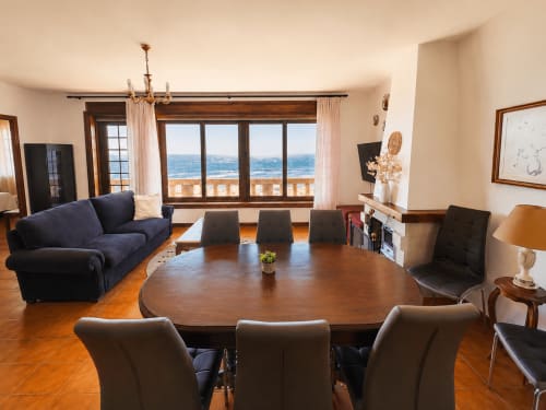 Amplia sala de estar en villa Vila Mar de Lua, Oia, con comedor, sofá azul marino, balcón con vistas al mar y vistas costeras