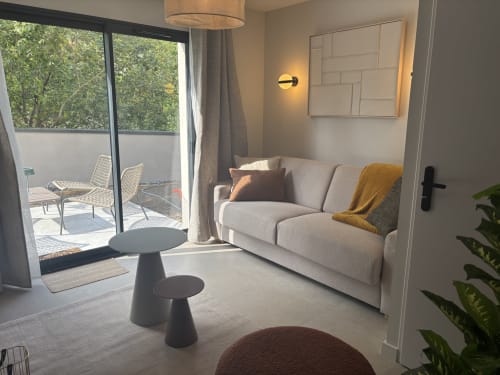 Séjour moderne à la Résidence Les 3 Volcans à Clermont-Ferrand avec vue sur le jardin, canapé beige et accès à la terrasse