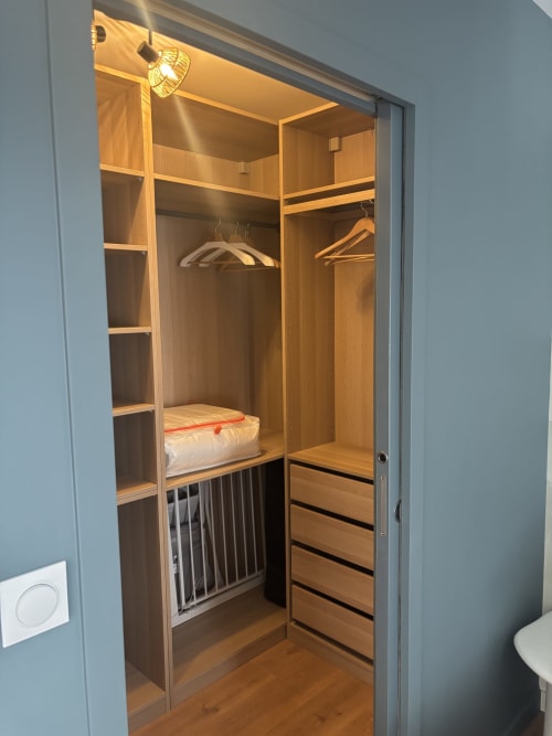 Dressing avec étagères en bois, cintres, paniers de rangement et éclairage chaleureux à Résidence Les 3, Puy de Dôme