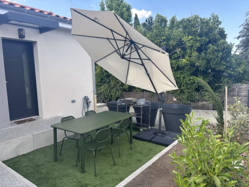 Patio moderne de la Résidence Les 3 Volcans avec table à manger, parasol suspendu, grill et vue sur le jardin à Clermont-Ferrand