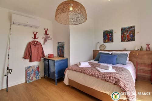 Chambre lumineuse du gîte Les écuries du bout du monde à Landunvez avec lit en bois, table de nuit bleue, lampe suspendue tressée